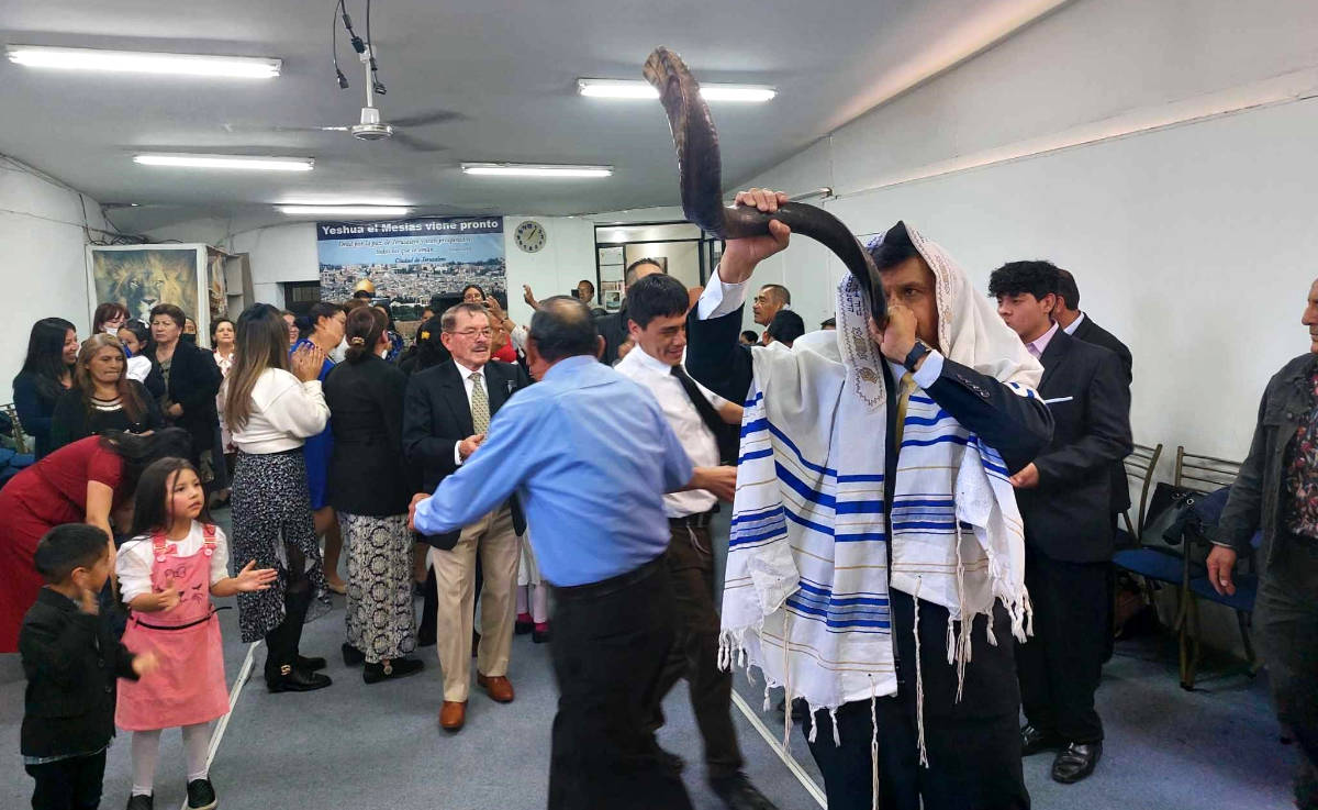 Man blowing shofar in a room full of people