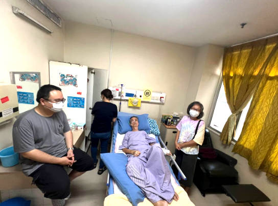 People sitting next to a person on hospital bed